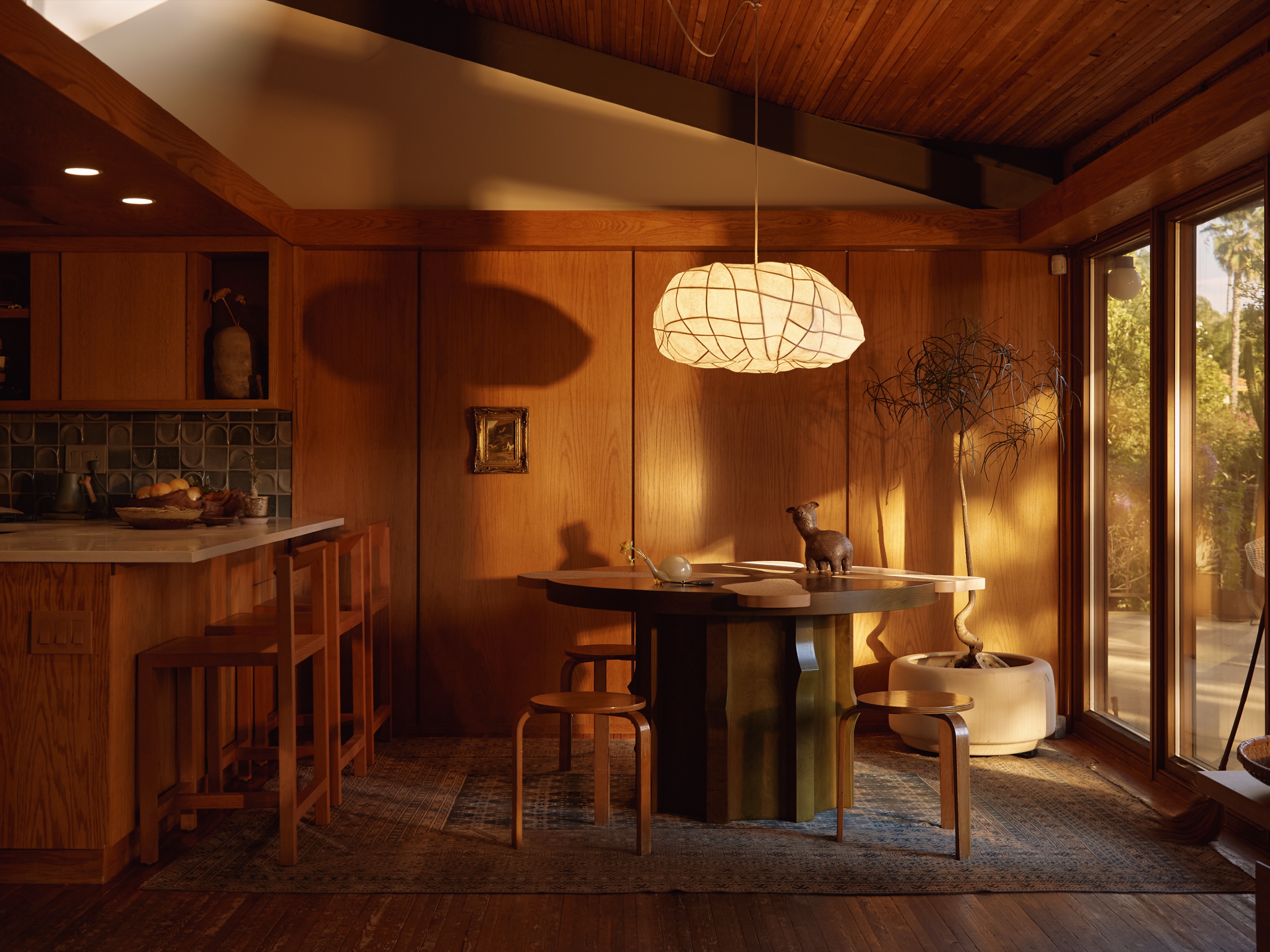 Dining nook with a cloud-shaped pendant over a sculptural table, oak paneling and floor-to-ceiling glass